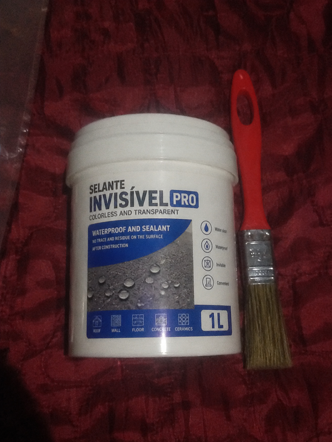 Balde de 1L do Selante Invisível PRO ao lado de pincel vermelho sobre tecido vermelho