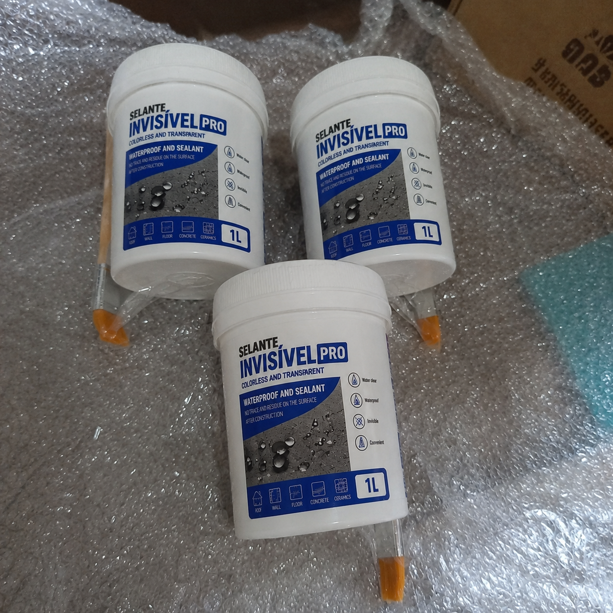 Três embalagens de 1L do Selante Invisível PRO com pincéis, embrulhadas em plástico bolha
